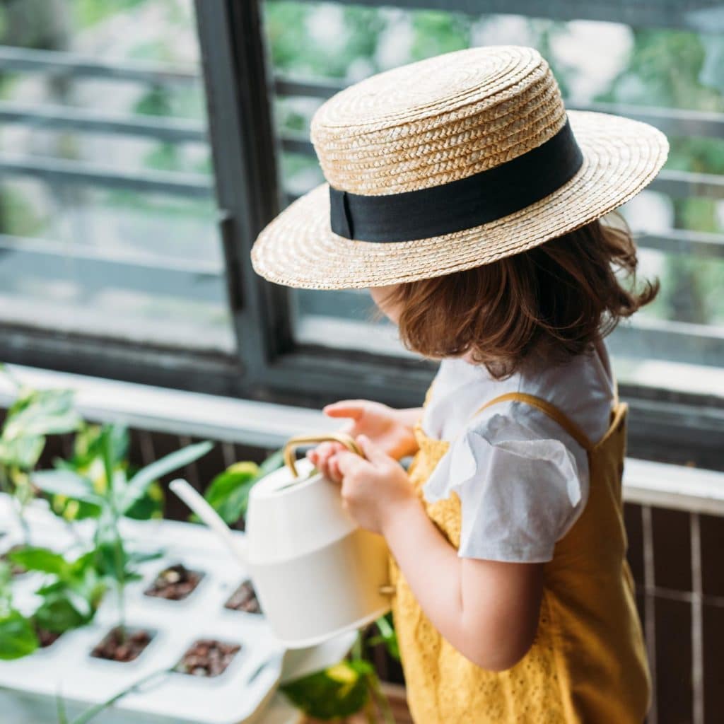 A child watering plants indoors with a watering can