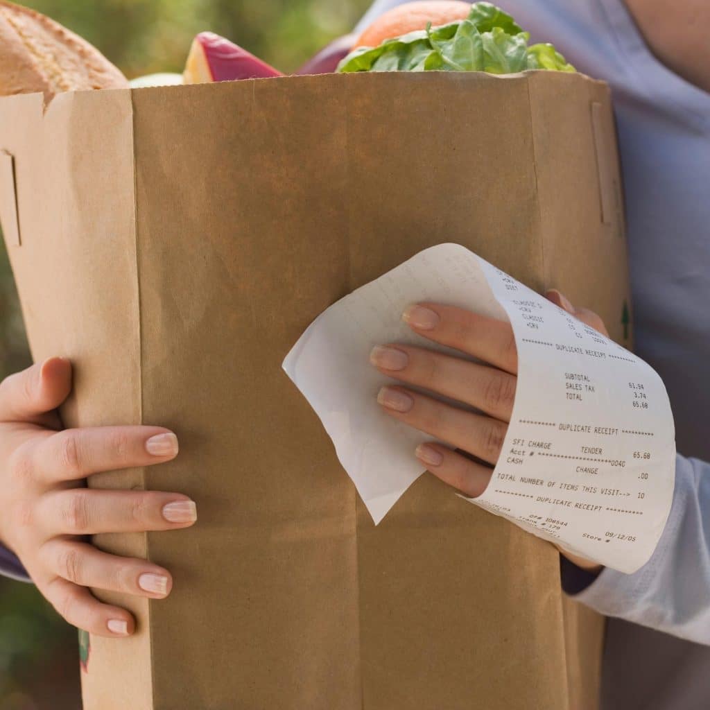 a lady holding a paper bag of groceries and her grocery receipt