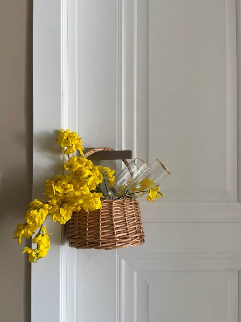 A basket of flowers against a white door hanging on the door handle.