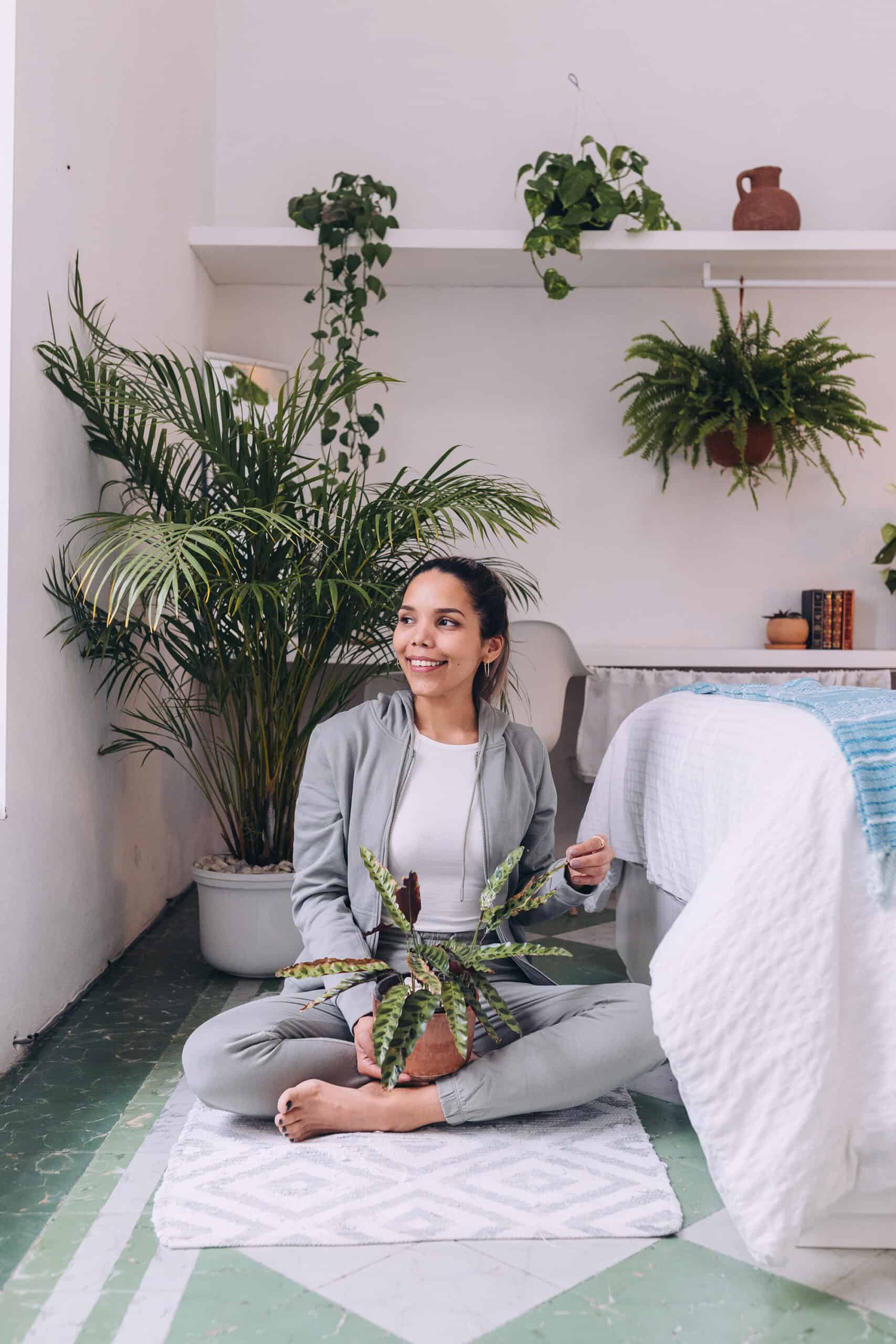 A woman sitting on the door smiling with a plant rattlesnake plant in her lap.